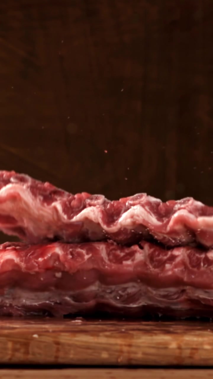 Costine di maiale crude che cadono su un tagliere di legno al rallentatore.