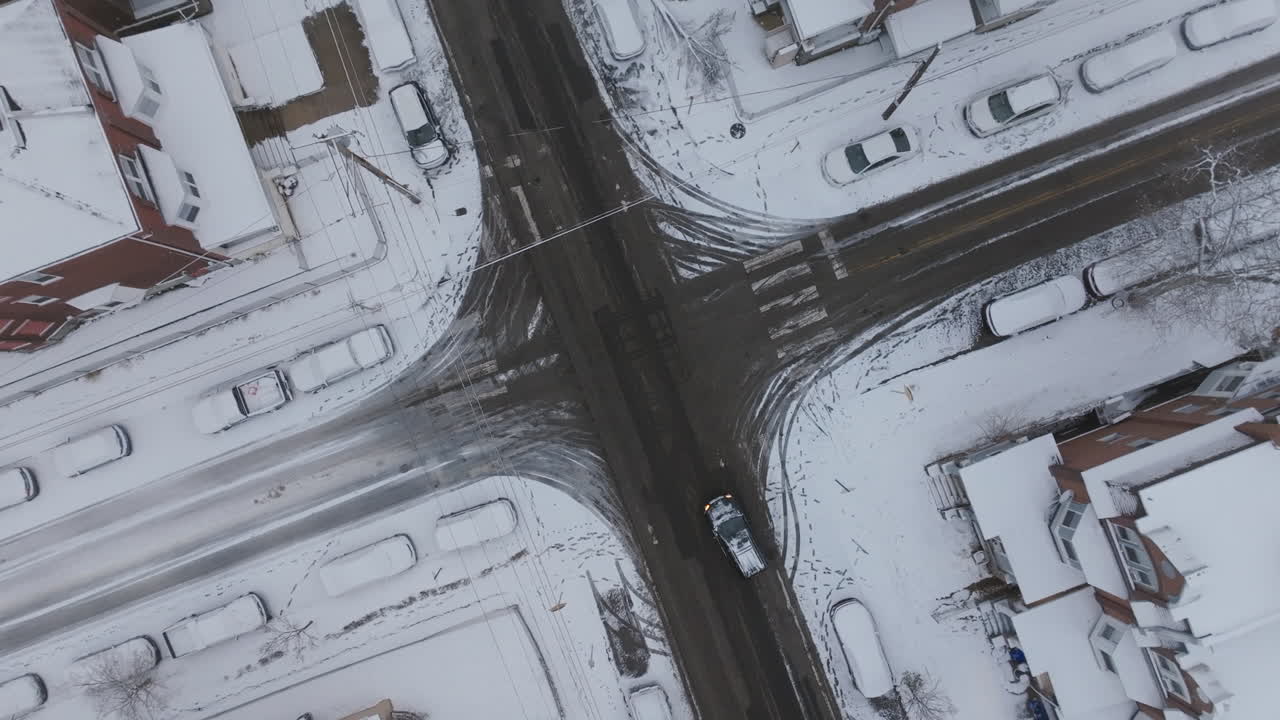Top down aerial footage that rotates around a road intersection in snow covered neighborhoods in West Philadelphia, Pennsylvania.
