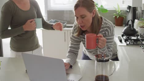 pareja de lesbianas caucásicas con tazas de café usando una computadora portátil en casa