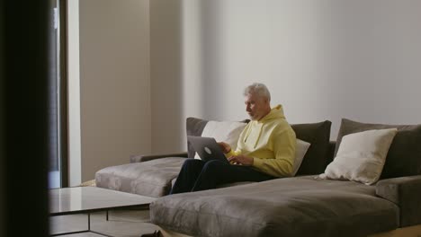 hombre mayor trabajando en una computadora portátil en una sala de estar moderna