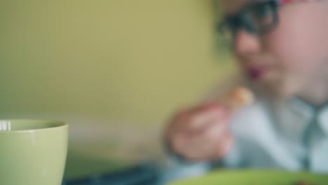 boy-bites-pizza-by-classmate-reading-book-at-table-in-room