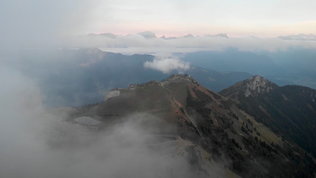 스위스 바우드 지방의 레이신 (leysin) 위의 구름을 통해 비행하는 다양한 산꼭대기가 스위스 알프스 산맥의 초록색 경사 위에서 다채로운 가을 해가 지는 동안 눈에 띄고 보이지 않습니다.