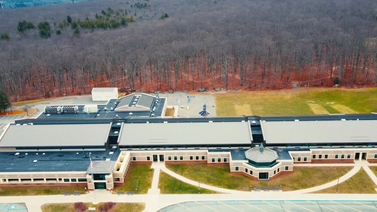A wide aerial pull-back drone shot capturing the full expanse of a large school campus in Scranton, PA. The modern building is surrounded by lush greenery, sports fields, and a dense forest backdrop.