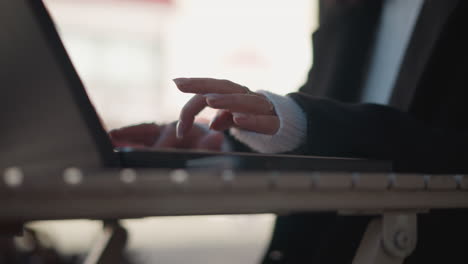 close-up of hands typing on laptop keyboard outdoors, featuring elegant manicured nails, rings, and cozy sweater sleeve, with soft natural light