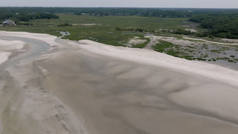 an estuary snakes toward the dunes and low houses, with flowing curves etched in silt and sand below wide skies