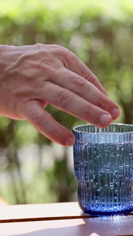 una mano exprime un limón en un vaso azul de refresco en una mesa al aire libre soleada