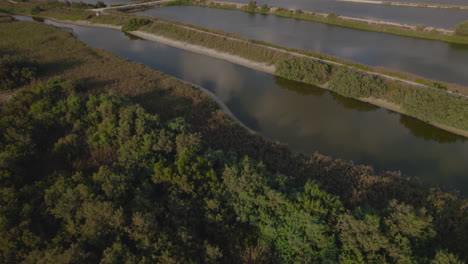 Aerial-view-of-fish-ponds-on-the-edge-of-a-natural-lake-at-the-foot-of-mountains,-a-vast-and-green-nature-reserve,-right-next-to-the-beach