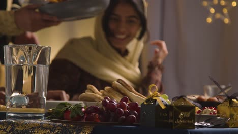 muslim family sitting around table with food for meal celebrating eid being served