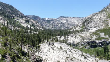 a slow pan 4k aerial drone shot moves down a rocky canyon in the california wilderness to reveal cliffs and trees and waterfalls as river runs through the valley on a sunny summer day with blue skies