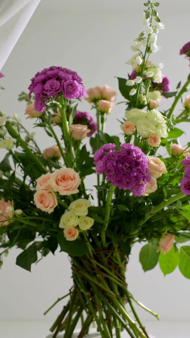 Video verticale: Tenda trasparente che scorre rivela un bouquet con steli intrecciati appeso alla parete.