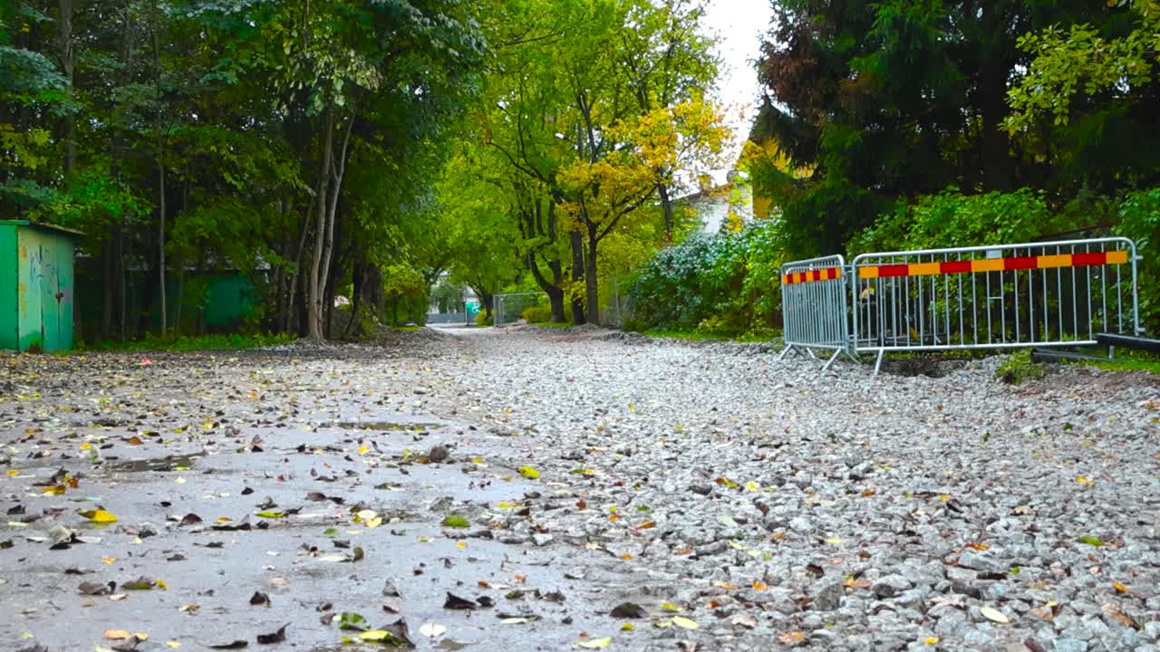 Road under construction with gray gravel on the ground during autumn time day light in Laagri or Pääsküla Estonia. Rainy day with rain fall in slow motion on the puddles on the muddy brown ground.