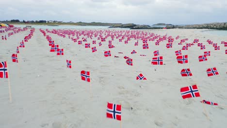 Lots-of-various-Norway-flags-in-rows-on-sandy-beach,-low-angle,-aerial-view-slow-flying-over