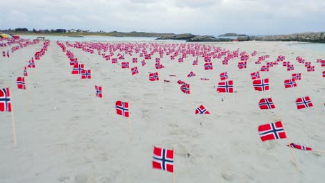 lots of various norway flags in rows on sandy beach, low angle, aerial view slow flying over