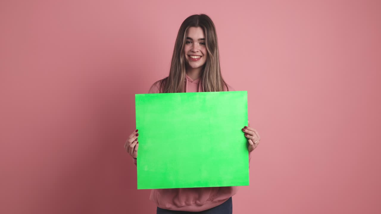Happy young woman with blank green paper in pink studio