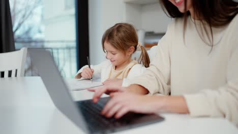 woman work on laptop while her daughter is painting at the table