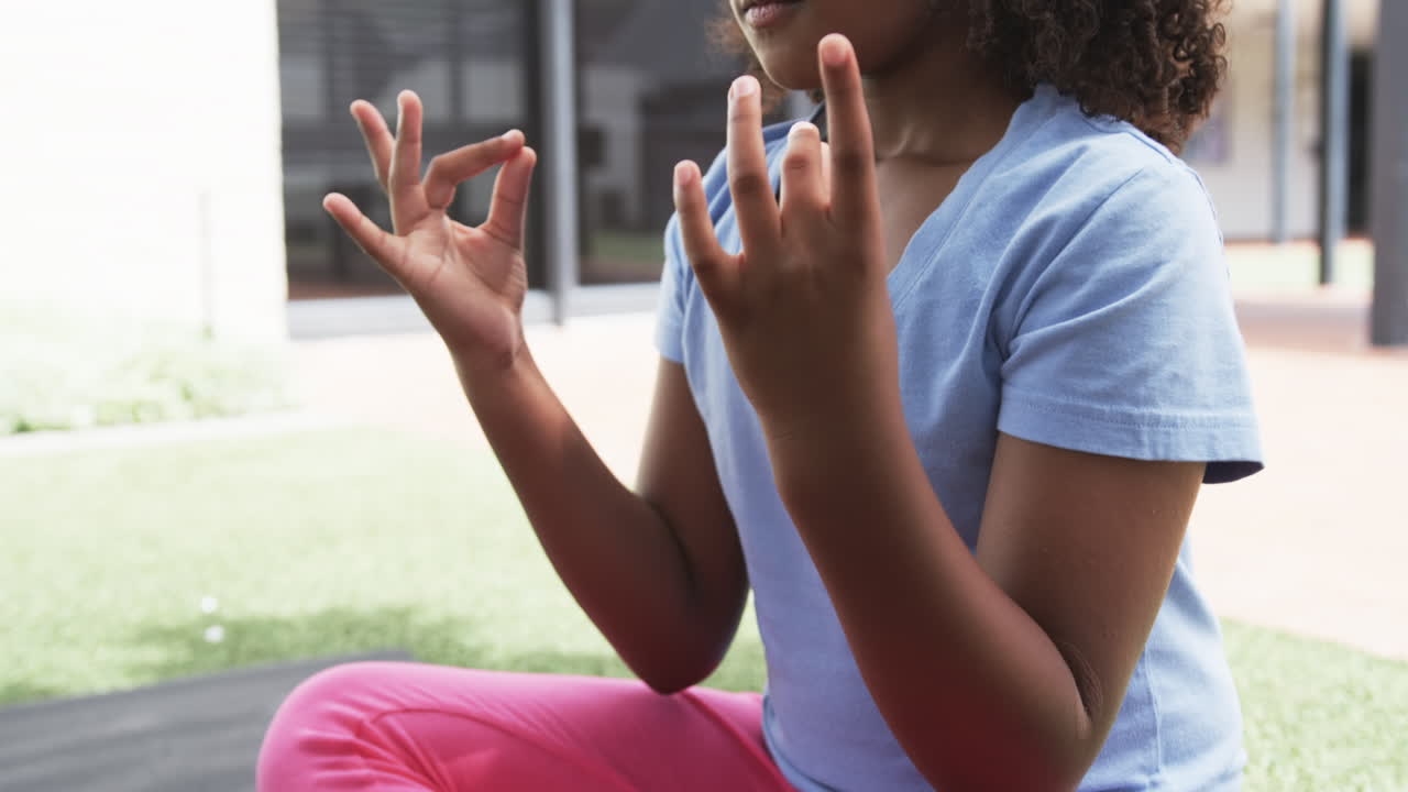 una chica biracial medita al aire libre, los dedos se tocan en una postura de mudra
