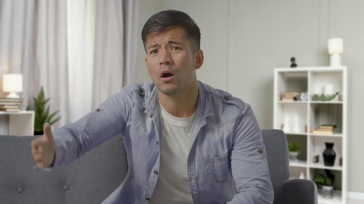 Shot Of Disappointed Young Man Sitting On Sofa At Home Watching Sport On TV As Team Loses