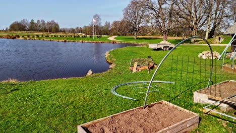 raised garden beds and lake on a sunny day, with diy arch trellis in progress