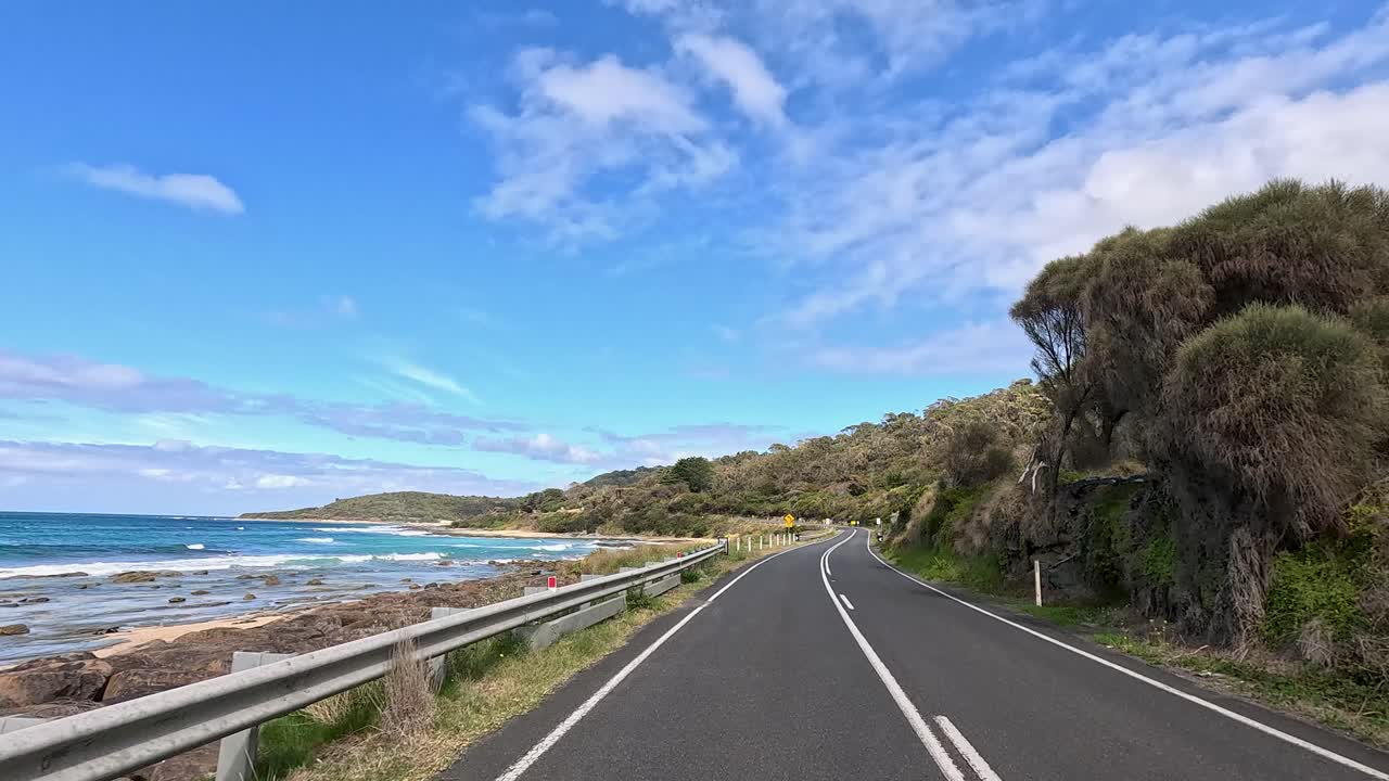 A picturesque drive showcasing coastal views, clear skies, and lush greenery along a winding road