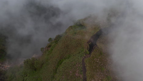 Close-up-tilting-aerial-view-of-a-broken-surface-at-the-top-of-a-mountain-ridge-on-an-active-volcano-surrounded-by-fog