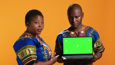 ethnic couple pointing at laptop with greenscreen display