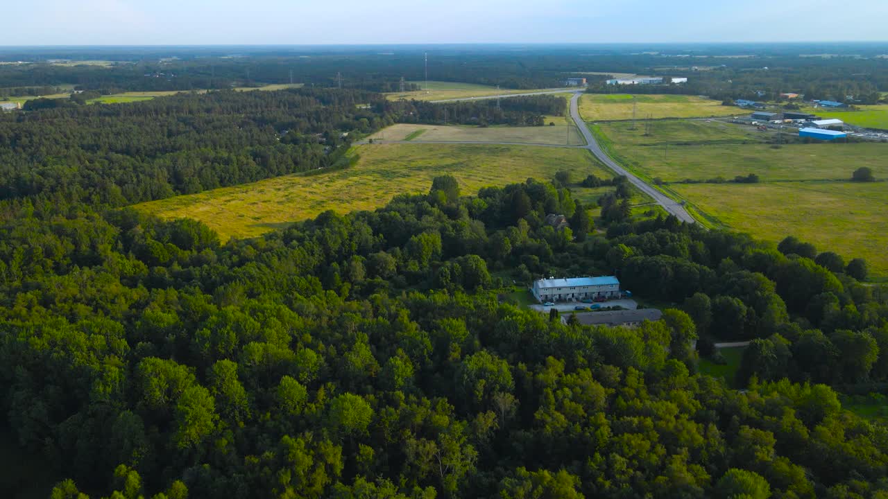 Aerial wide orbit above rural Saku countryside landscape during a golden summer evening. Highway lonely road cutting through farmlands with expansive wooded areas, green forests and farming structures