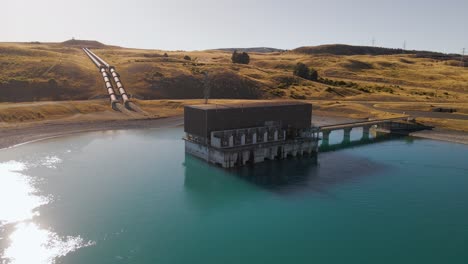 Hydroelectric-power-plant-on-shore-of-blue-lake-in-morning-sunlight