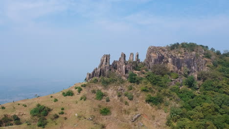 drone circles around large rocky mountain of ghambhirgad fort, maharashtra, with clear blue sky in background