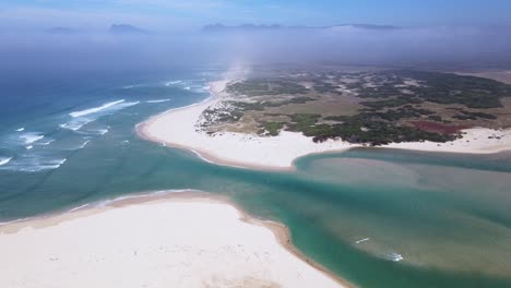 Dramatische-Drohnenszene-Einer-Flussmündung,-Die-Sich-Zum-Meer-Hin-öffnet,-Mit-Sanddünen-Und-Bergen-In-Der-Ferne