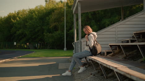 female coach in casual attire with black bag sits on stadium bleachers, adjusting her bag thoughtfully, she appears focused and prepared