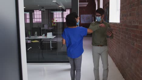 Diverse-race-male-and-female-business-colleagues-greet-with-elbows-wearing-face-masks