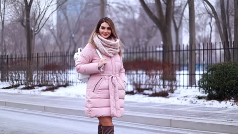 woman in pink puffer coat and white backpack walking in a snowy winter setting