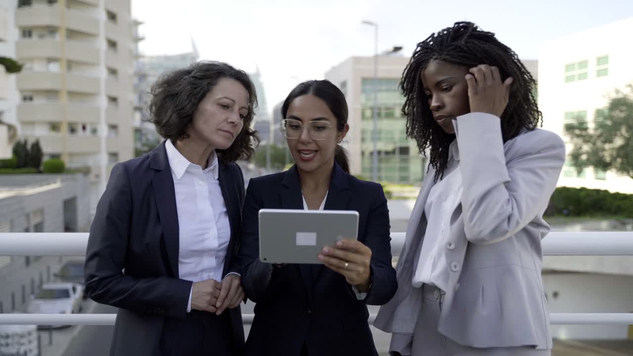 Mujeres sonrientes con trajes mirando una tableta