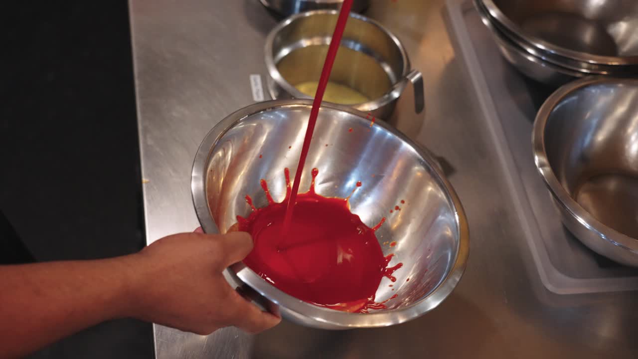 Riprese in slow motion 4K di salsa piccante per alette versata a filo con un mestolo in una ciotola di miscelazione in acciaio inossidabile, catturando la ricca consistenza, il colore vivido e la preparazione della salsa in una cucina