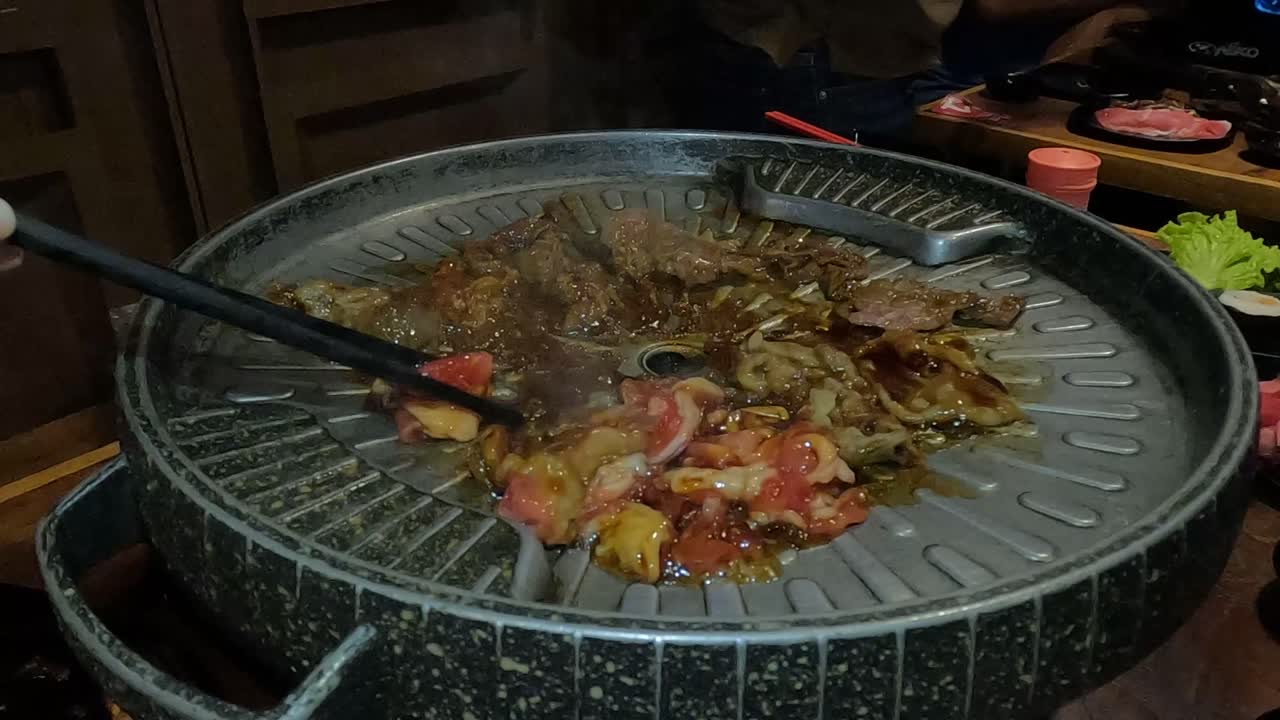 People prepare meat on Korean barbecue in restaurant, close up