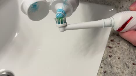 generic shot of white caucasian hand applying toothpaste onto electric toothbrush preparing for brushing teeth