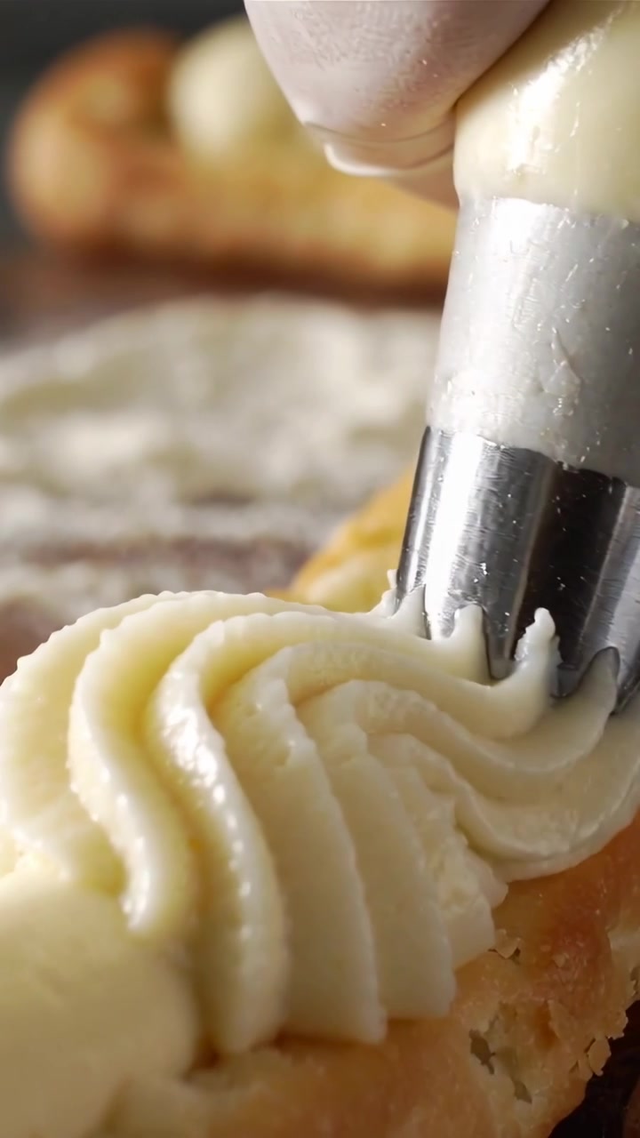 Vertical video: Pressing bag gloved hand piping cream from star nozzle onto split shell, decorating