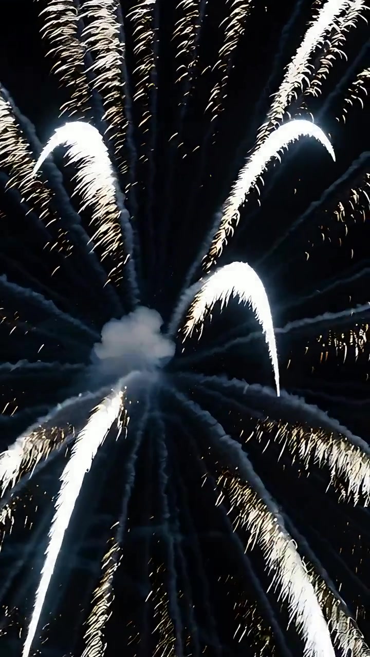 Vertical video: Flashing core igniting white-gold burst, sending gold trails and smoke in night sky