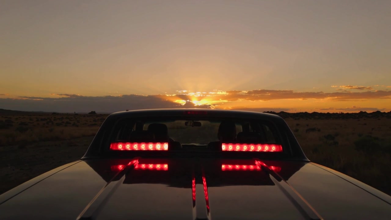 Inquadratura del posteriore di un'auto al tramonto sul ciglio della strada, con la telecamera che registra il sole che scende per catturare i riflessi dei LED.