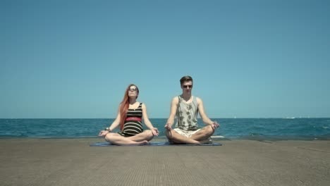 Young-couple-meditating-sitting-on-pier-by-beach.-Holidays-with-yoga-classes