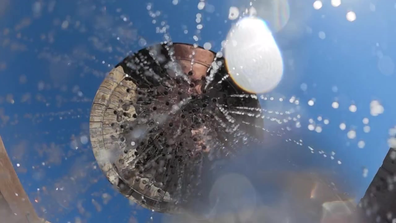 明るい日差しと澄み切った青空を背景に、水しぶきと無数の水滴が抽象的なボケ効果を生み出している。