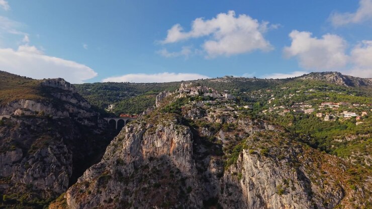 Ripresa aerea in avvicinamento del borgo medievale di Eze Village in cima a una collina con gola rocciosa, ponte viadotto e montagne, terreno drammatico della Costa Azzurra, paesaggio scenografico della Francia