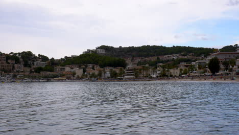 the beach of port d’sóller, mallorca, seen from the pier with the city and mountains in the background