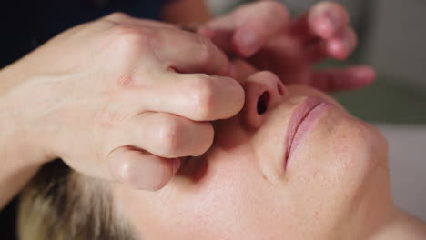 close up of participant lying face up on massage bed as bodywork therapist uses gentle circular motions to massage brows and forehead, smoothing skin, releasing tension in spa environment