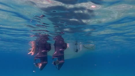 Slowmotion-under-water-scene-of-human-legs-and-feet-in-sea-water-beneath-surface-protruding-from-motorboat-ladder