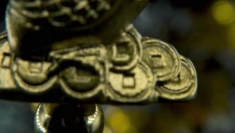 Chinese-New-Year-traditional-golden-chicken-zodiac-statue,-hanging-shiny-gold-rooster-sitting-on-money-coins-Asian-symbol,-glowing-background-with-blurry-depth-of-field,-cinematic-macro-tilt-up-4K