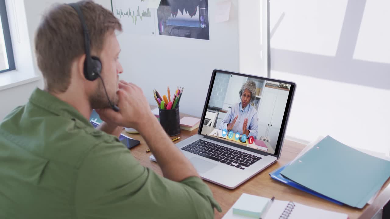 Kaukasisk mand bruger bærbar computer og telefonheadset på videoopkald med en kvindelig kollega.