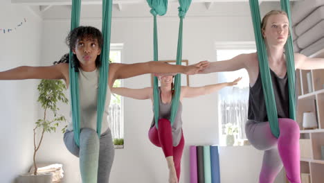 focused diverse fitness teenage girls exercising in aerial yoga class in big white room, slow motion