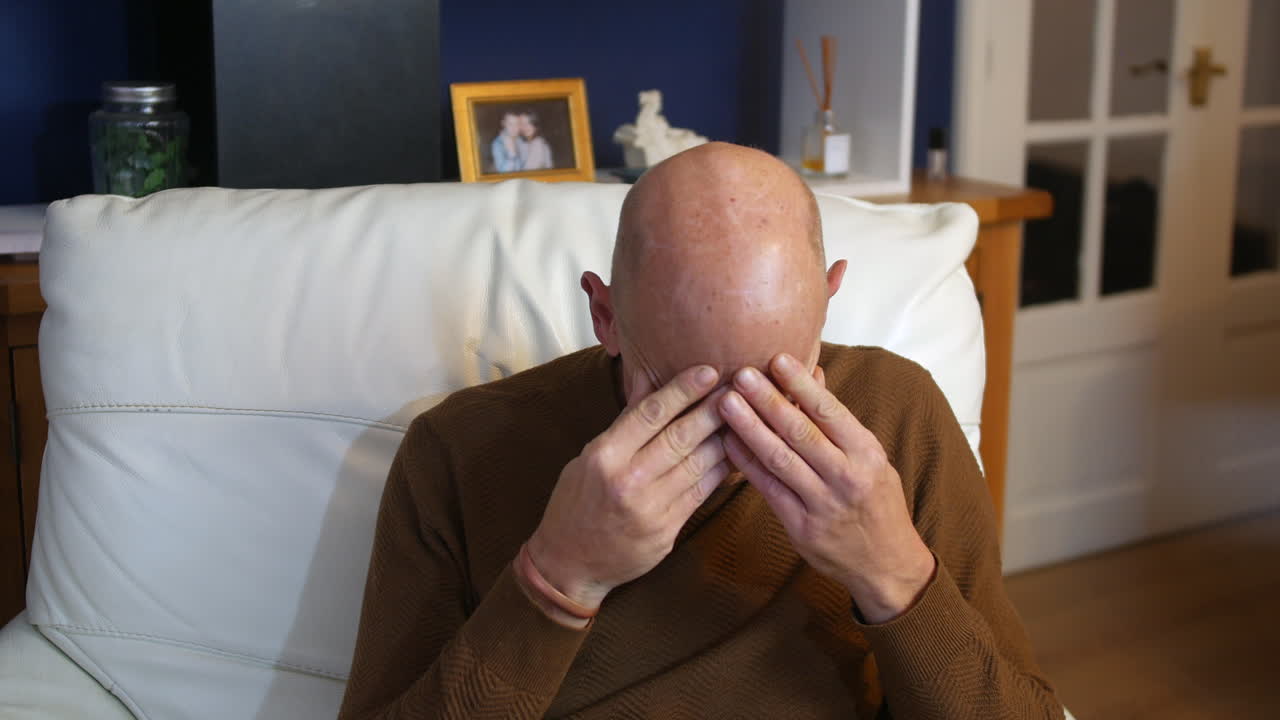 Un uomo calvo maturo, frustrato e turbato, a casa nel suo salotto, con aria confusa e arrabbiata