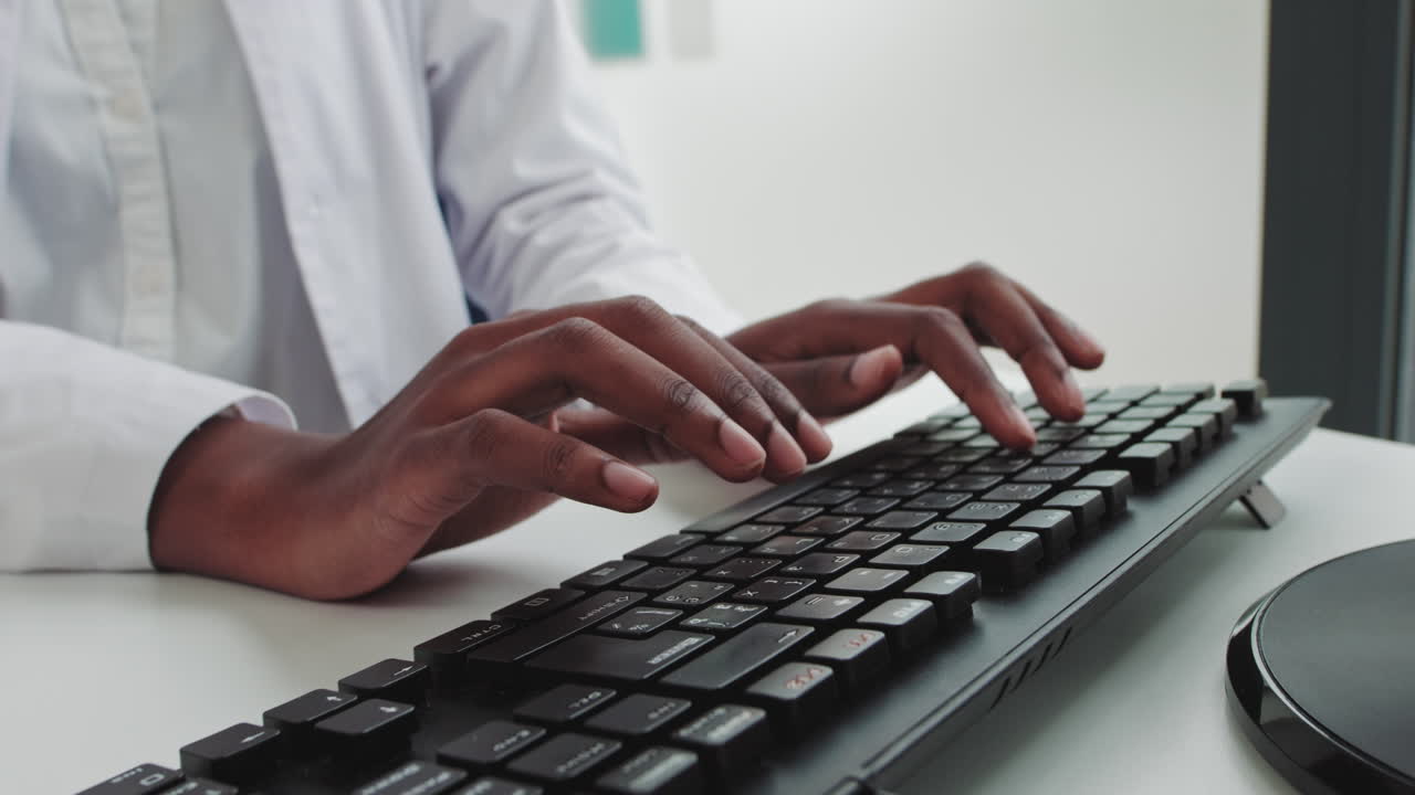 Close up of hands of young african woman in medical uniform typing on keyboard in hospital